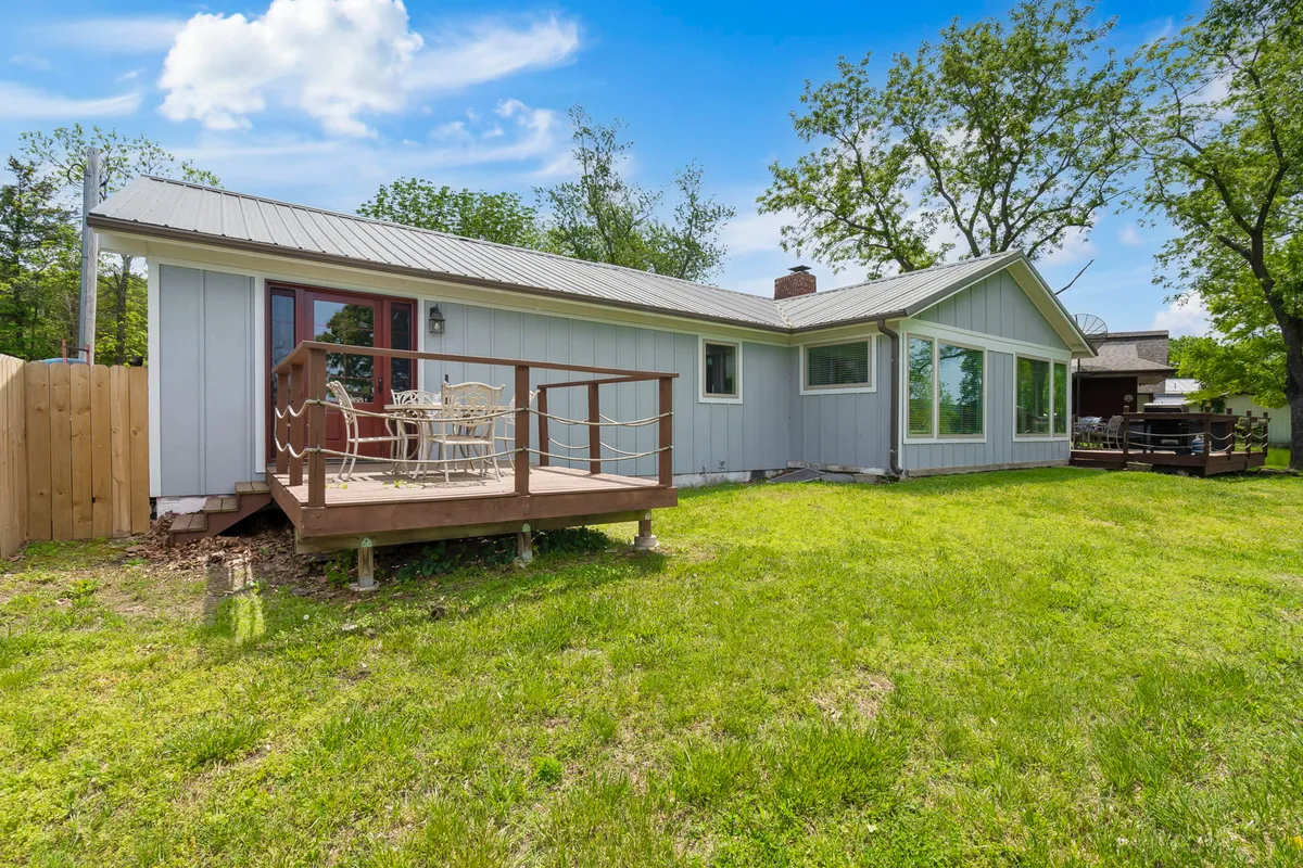 A welcoming wooden deck equipped with outdoor seating, set adjacent to a vibrant grassy area. The large windows and open design create an inviting transitional space for both people and pets to enjoy fresh air, sunshine, and activities.