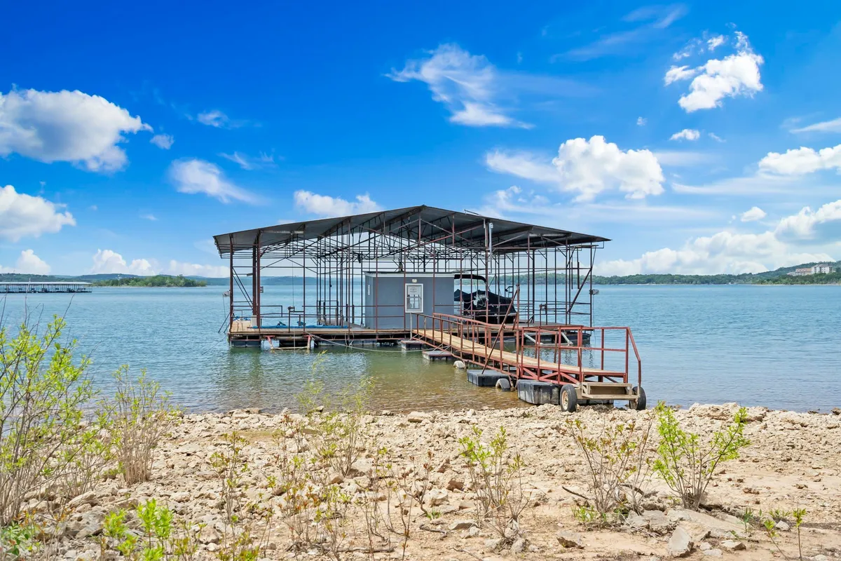 A peaceful dock extending over the water, with a boat lift visible and tranquil water reflecting the sky. The scene is framed by blue skies and gentle waves, suggesting a variety of lakeside activities possible throughout the year.