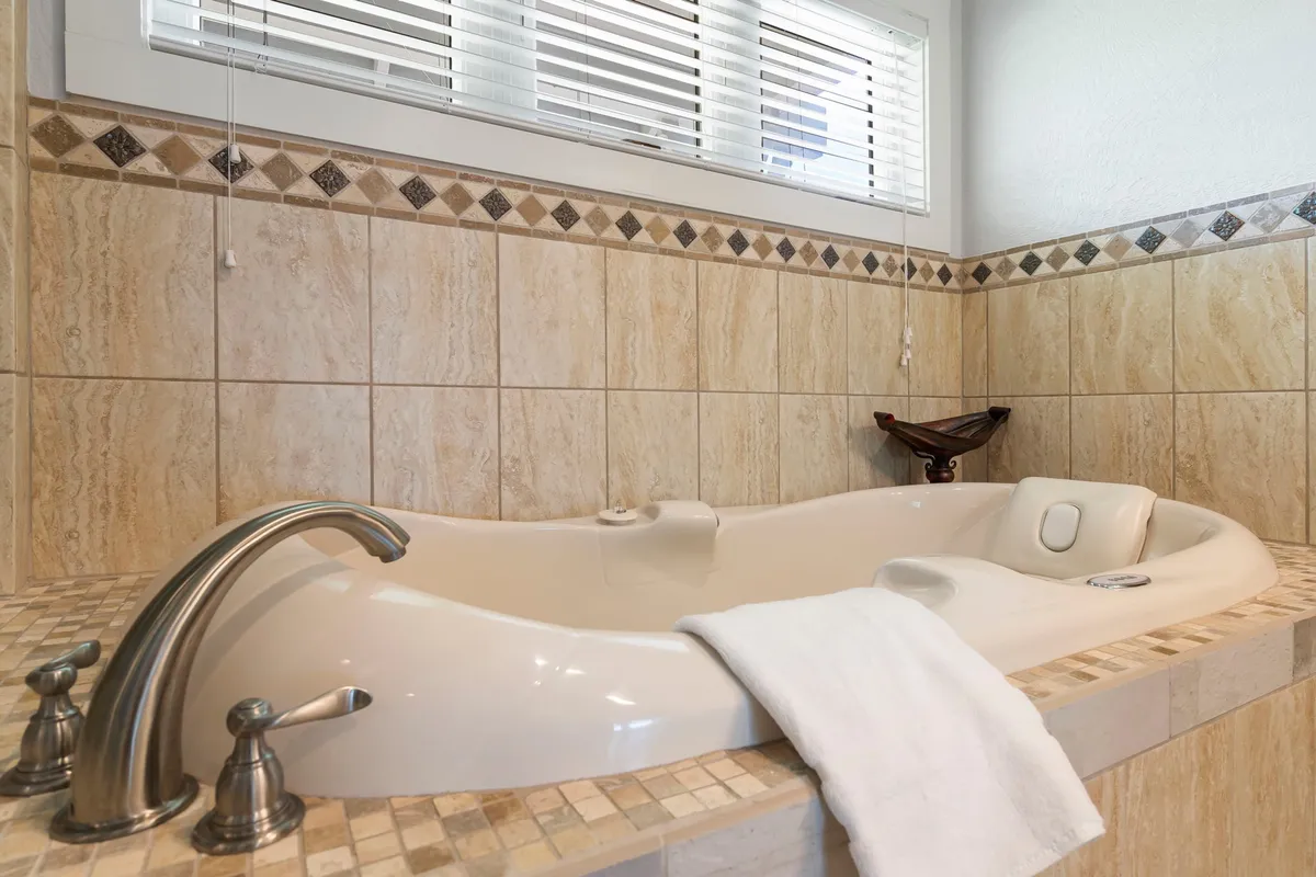An inviting bathtub with elegant decorative tile work and a fresh, white towel set the scene for a calming soak. The understated color palette and tranquil atmosphere create a spa-like experience, ideal for moments of relaxation and self-care.