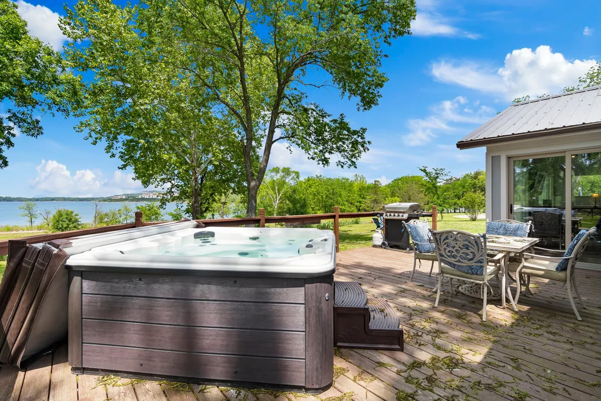 An exterior shot of the expansive back deck, showcasing the inviting hot tub, outdoor dining set, and a clear view of the lake. The scene suggests relaxation and celebration, with space for barbecues, stargazing, and soaking in the serene surroundings.