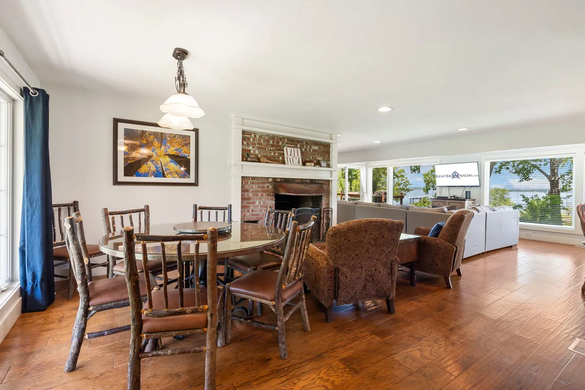 A warm dining area with a large wooden table surrounded by comfortable seating, positioned near expansive windows that offer beautiful views of the lake. The fireplace adds a touch of coziness, underscoring the inviting ambiance for family meals and celebrations.